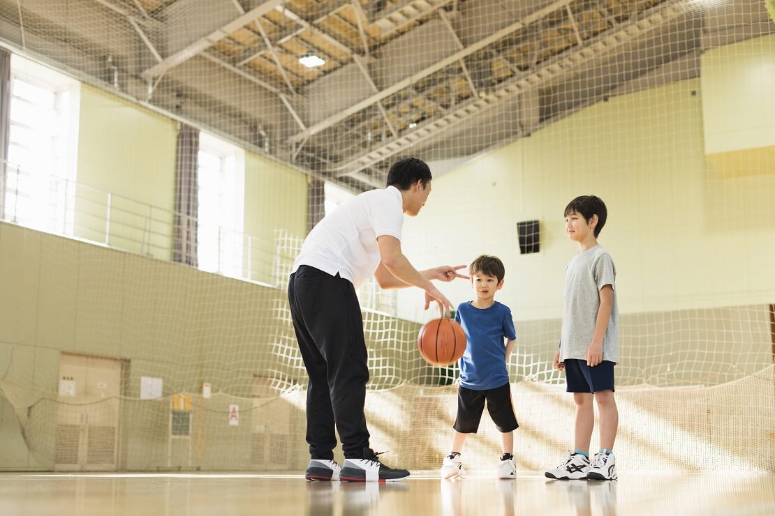 Basketballcoach steht mit einem Ball vor zwei Kindern