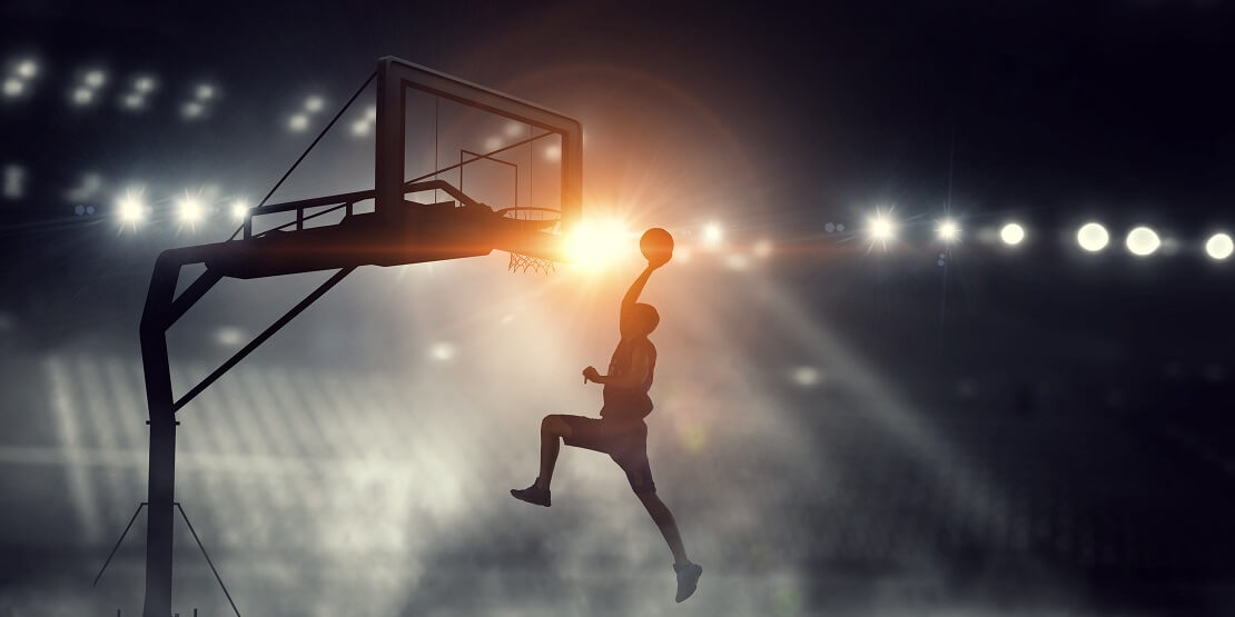 Ein Basketballer beim Dunking vor leeren Raengen