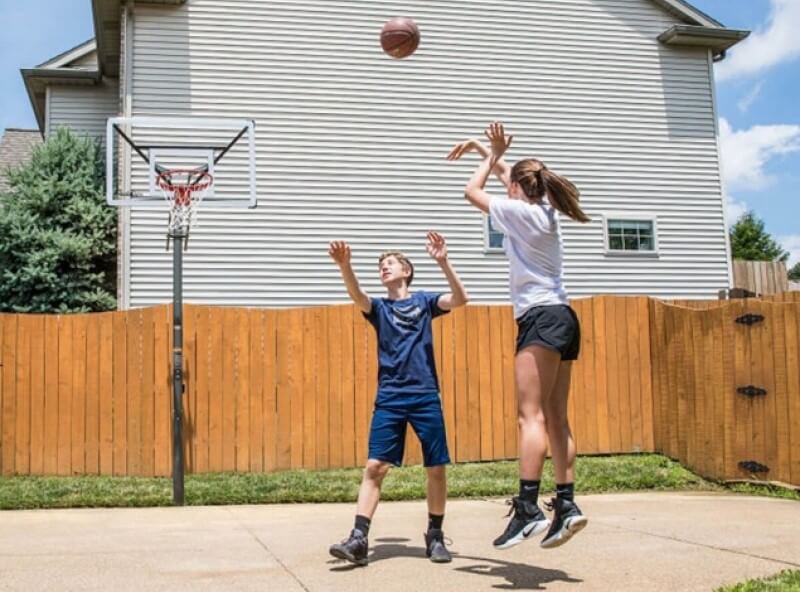 Ein Mädchen wirft auf einen heimischen Basketballkorb, ein Junge versucht zu blocken