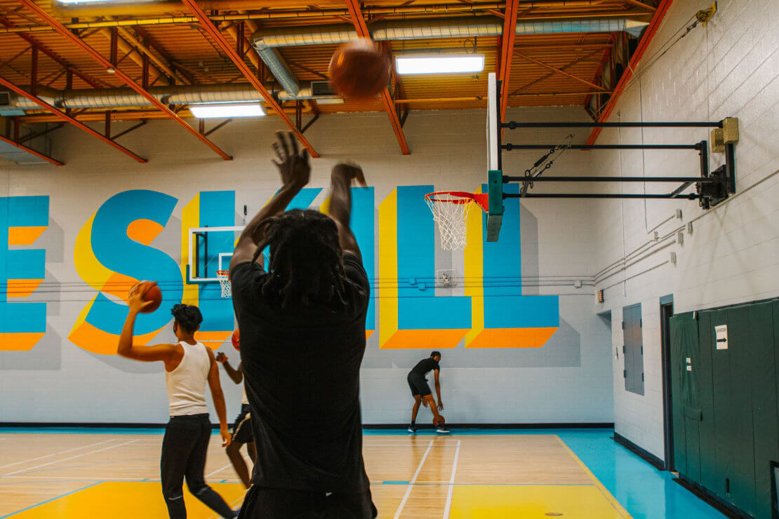 Ein Basketballer mit Dreadlocks wirft einen Ball auf einen Korb