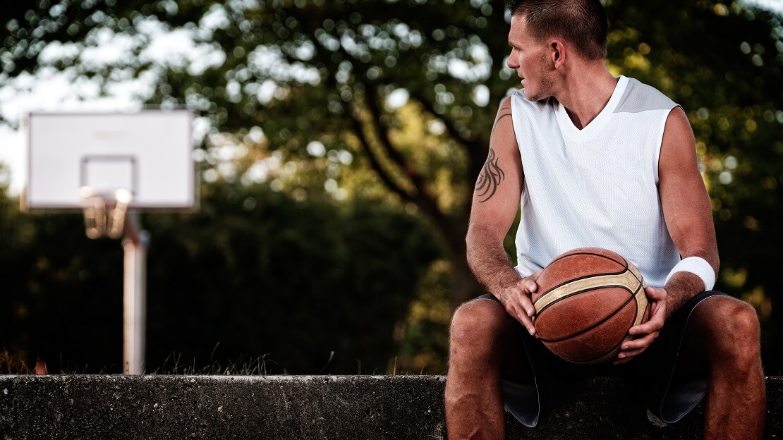 Ein basketballer sitzt auf der Bank und schaut zum Korb