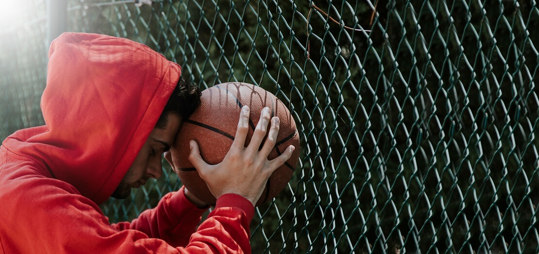 Basketballer lehnt am Zaun