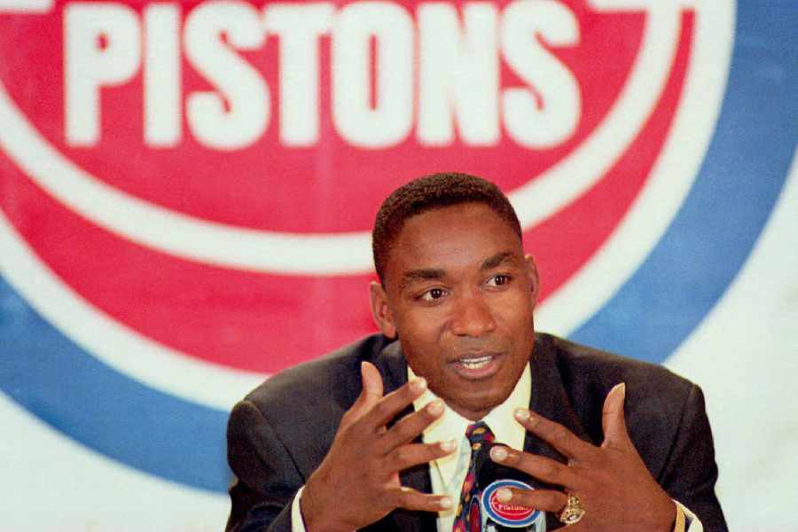 Isiah Thomas im Anzug bei einer Pressekonferenz, dahinter das Logo der Detroit Pistons