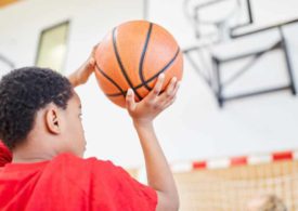 Ein Kind ist kurz davor ein Basketball in den Korb zu werfen