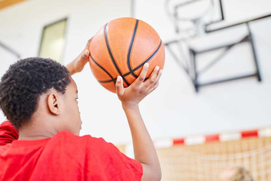Ein Kind ist kurz davor ein Basketball in den Korb zu werfen