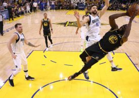 Draymond Green in der Luft, probiert den Ball in den Korb zu werfen. Dallas Spieler blocken ihn.