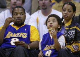 Ice Cube sitzt mit Frau und Kind in Lakers-Klamotten auf der Tribüne