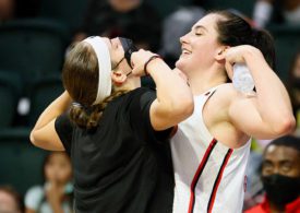 Eine Basketballspielerin und eine Trainerin stehen sich gegenüber und führen ein Jubel durch, wobei sie beide ihren Bizeps anspannen