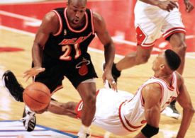 Zwei Basketballspieler spielen gegen einander und einer fällt auf den Boden