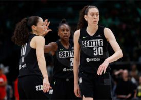 Drei Basketballspielerinnen in schwarzen Trikots klatschen sich ab