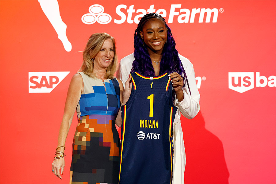 Die Basketballspielerin Aliyah Boston hält ein Trikot hoch und steht neben Cathy Engelbert