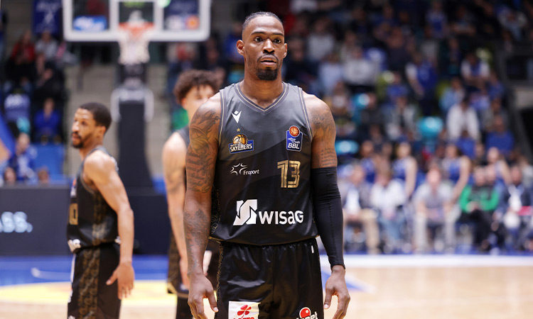 Ein Basketballspieler der in einem schwarzen Trikot in der Mitte des Bildes steht