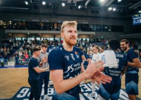 Der Basketballspieler Max Ugrai von der Mannschaft MPL Academics Heidelberg klatscht in seine Hände und im Hintergrund sieht man seine Mannschaft