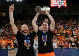 Zwei Basketballspieler Jubeln und einer von ihnen hält kein Pokal mit beiden Händen hoch