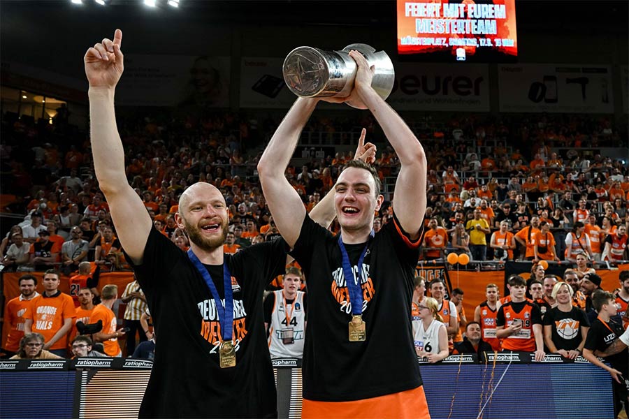 Zwei Basketballspieler Jubeln und einer von ihnen hält kein Pokal mit beiden Händen hoch