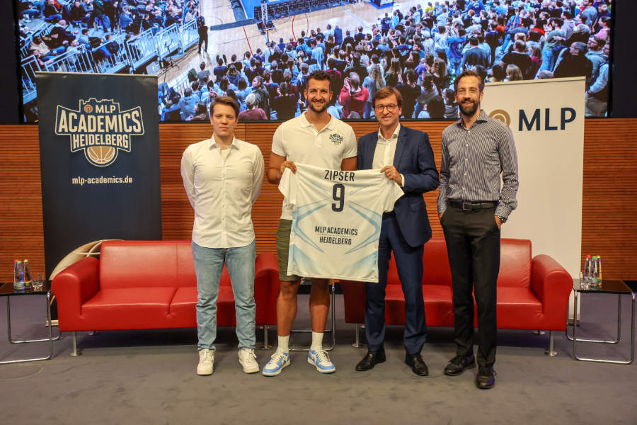 Ein Basketballspieler und Vereinsfunktionäre halten ein neues Trikot hoch