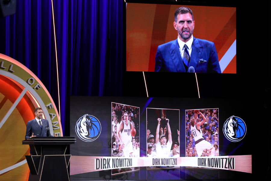 Dirk Nowitzki an einem Redepult bei seiner Aufnahme in die Hall of Fame, rechts neben ihm Bilder aus seiner Karriere