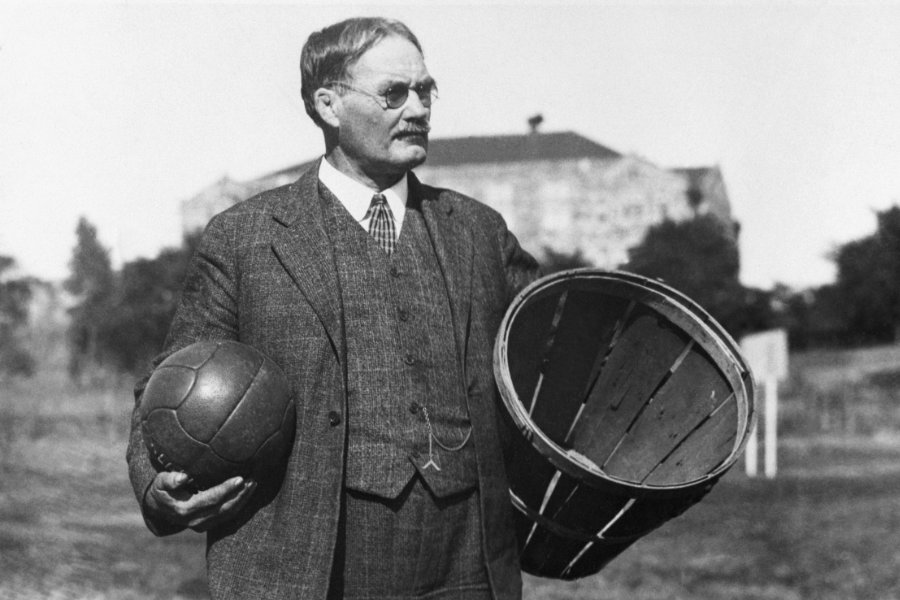 Dr. James Naismith mit einem Ball in der rechten und einem Korb in der linken Hand