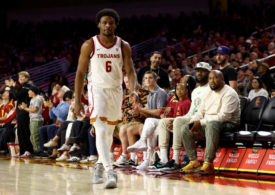 Bronny James von den USC Trojans läuft auf dem Basketballcourt. Im Hintergrund sitzt LeBron James auf den Zuschauer-Bänken.