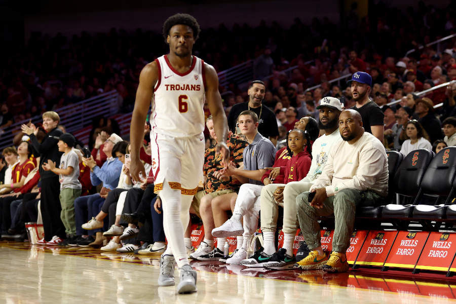 Bronny James von den USC Trojans läuft auf dem Basketballcourt. Im Hintergrund sitzt LeBron James auf den Zuschauer-Bänken.