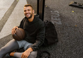 Ein junger Mann lehnt mit einem Basketball in der Hand an einem Pfosten