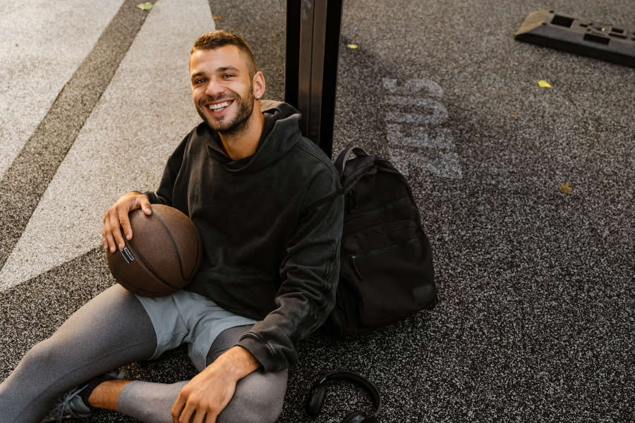 Ein junger Mann lehnt mit einem Basketball in der Hand an einem Pfosten